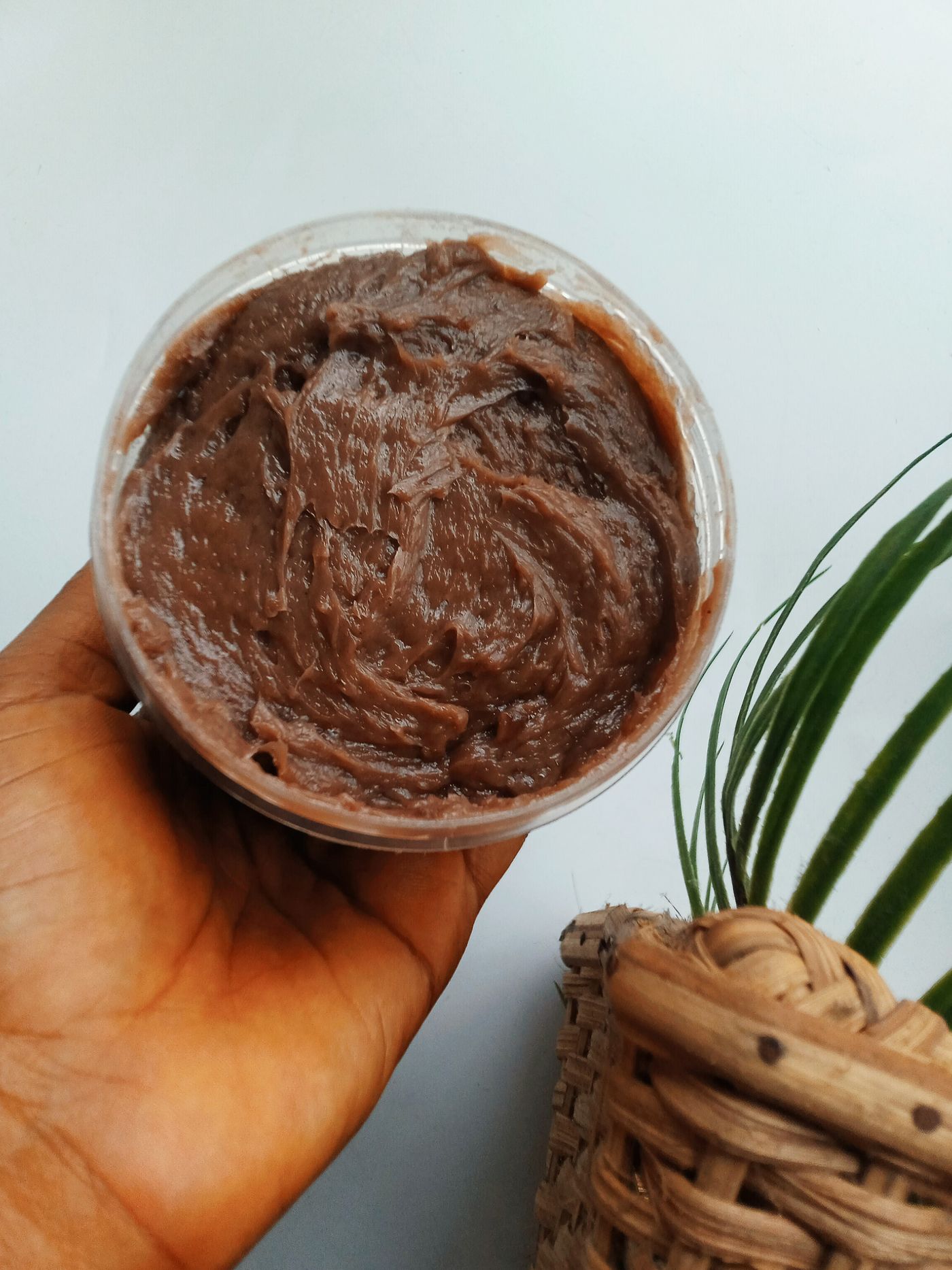 Unrefined shea butter held in an open hand beside a woven basket, showing the soft ivory texture of raw shea